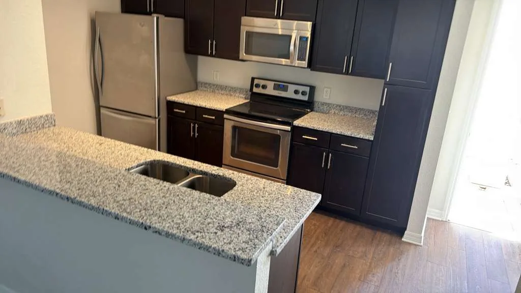 Granite kitchen counter with a double sink, dark cabinets and a stainless range