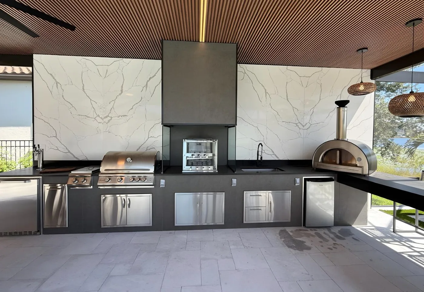 Outdoor kitchen with a stone slab backsplash, built in grill and a pizza oven